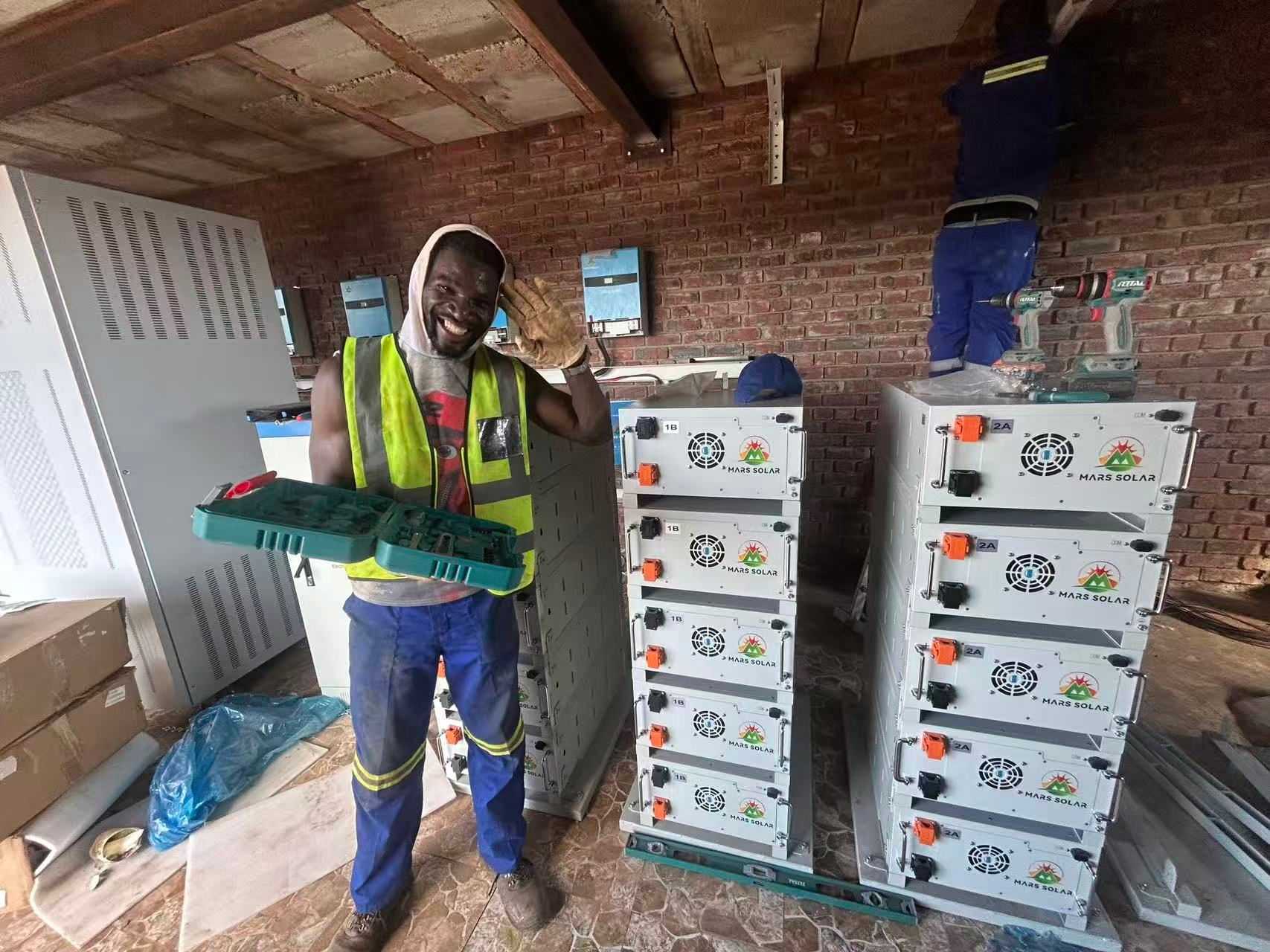 Mars Solar engineer installing branded lithium battery modules on a rack during a solar project in Ghana