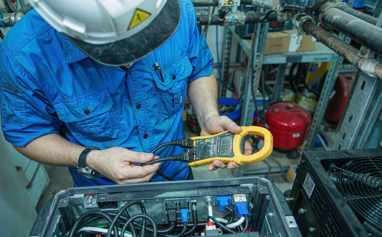 Technician commissioning a hybrid inverter sizing check with a clamp meter