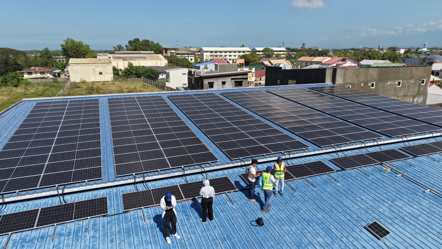 Drone aerial view of a completed rooftop solar array with installation crew, Mars Solar project in the Philippines